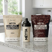 mëtta complete protein on countertop with mëtta shaker. vanilla and raw cacao complete protein. 